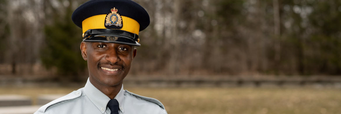 Black male RCMP officer stands outside smiling. 