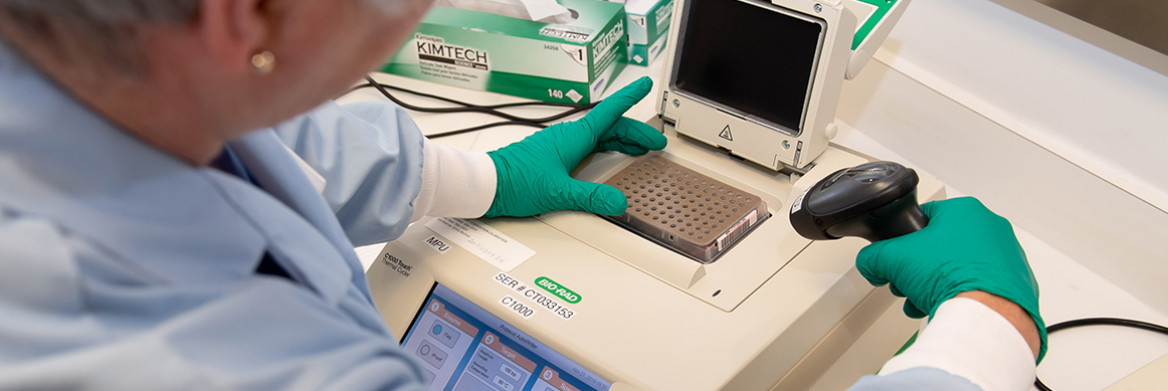 Une femme travaillant dans un laboratoire et vêtue d'un sarrau et de gants.