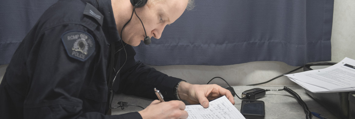 Un agent de la GRC portant des écouteurs rédige des notes, assis à un bureau. 