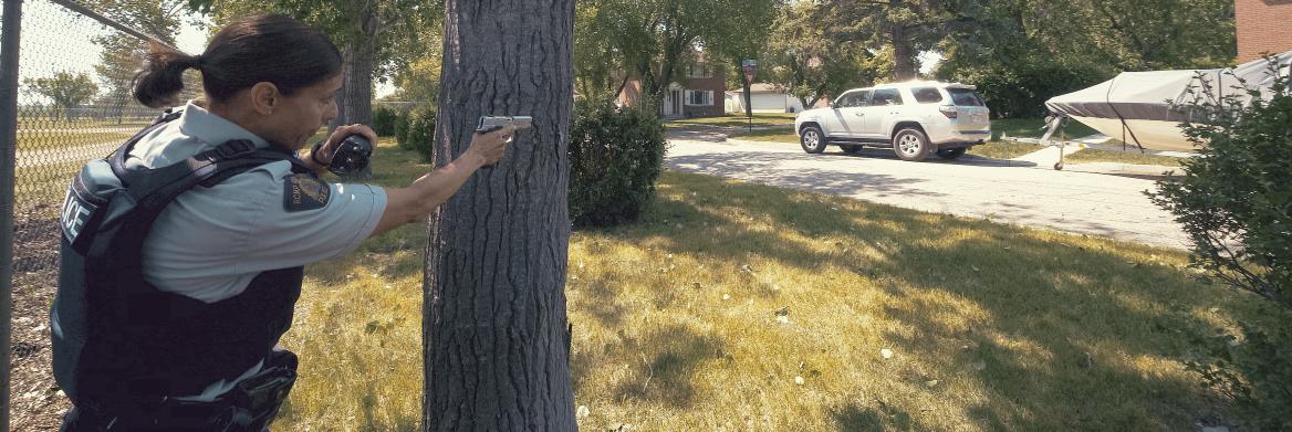 Femme policière braquant son arme à l'extérieur.