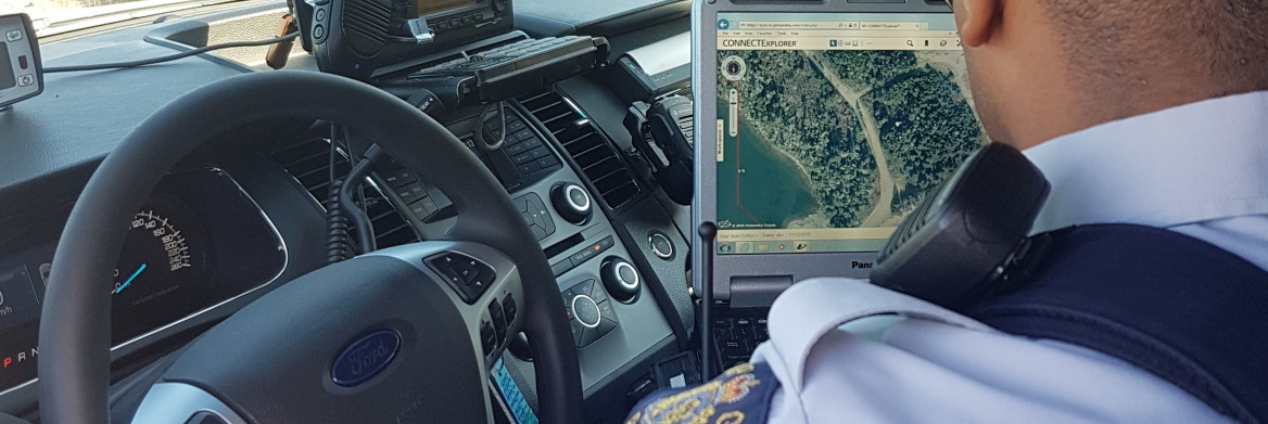 Male police officer sits in front of computer with map on screen.