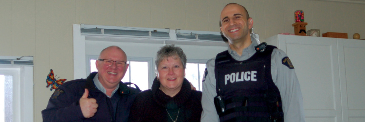 A man, a woman and a male police officer stand in a living room.