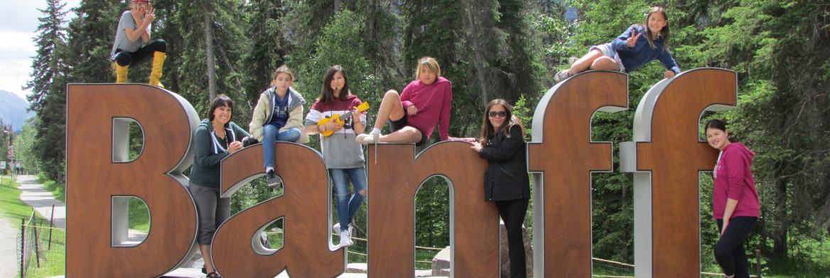 Sept fillettes et une adulte autochtones à l'extérieur prennent la pose en s'amusant sur les lettres géantes B-A-N-F-F.