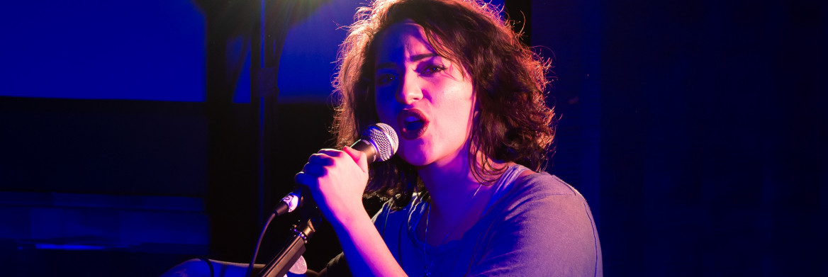 A young woman sings into a microphone.