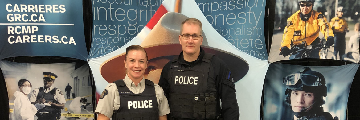 One female and one male RCMP officer stand behind a recruiting booth.