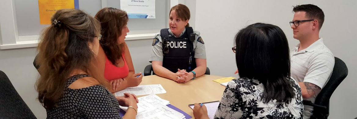 Three women and a man sit around a table with a female police officer