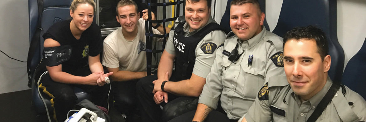 One female and four male police officers in t-shirts sit in back of ambulance.