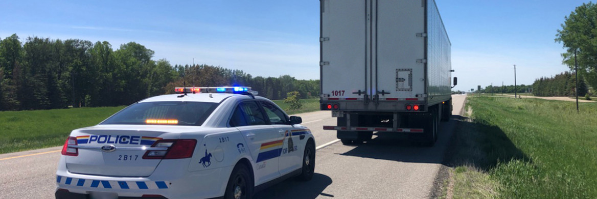 An RCMP cruiser parked on the side of a highway behind a transport truck. 