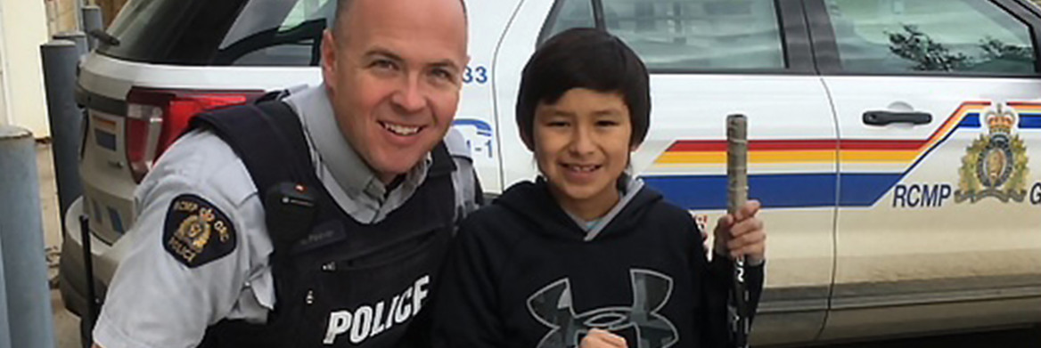 Un policier de la GRC debout à côté d'un garçon tenant un sac et un bâton de hockey.