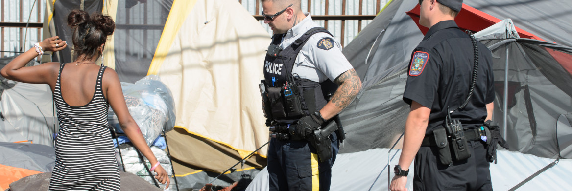 Un policier parle à une femme devant des tentes.