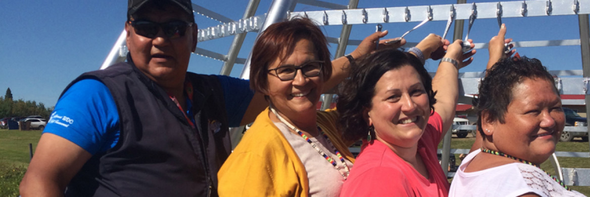 Onion Lake community members stand next to a large steel teepee.