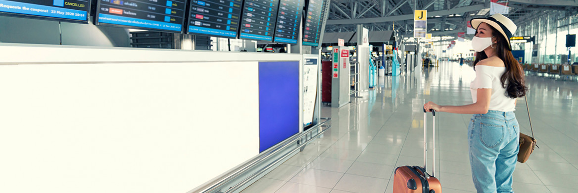 A female traveller holding a suitcase looks up at an airport flight information board.