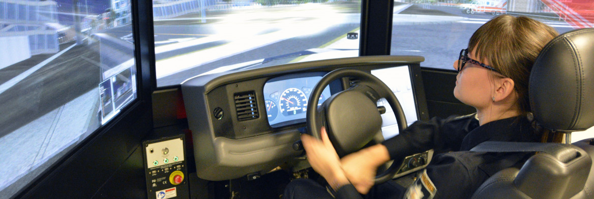 Female police officer sitting in front of screen holding a driving wheel.
