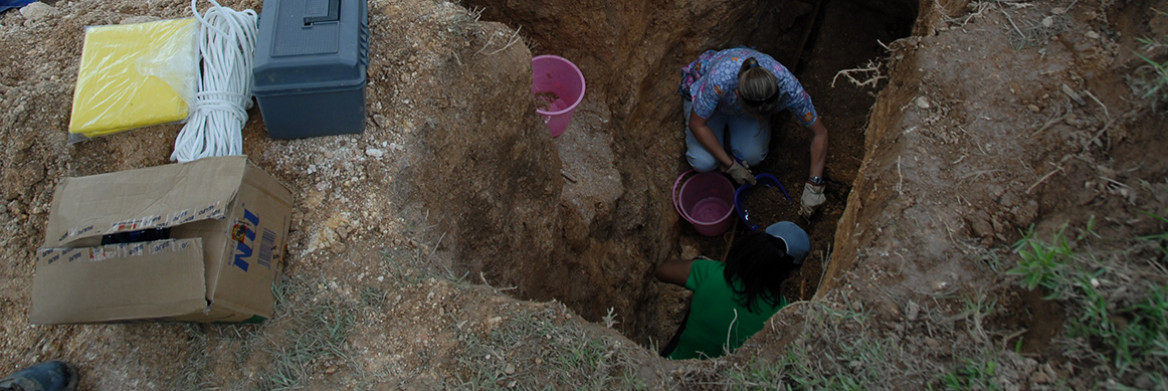 Two women collect evidence from a deep hole in the ground. 